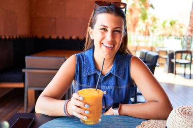 Genç ve güzel bir kadın restoranda oturmuş yaz tatilinin tadını çıkarıyor sağlıklı meyve suyu içiyor.