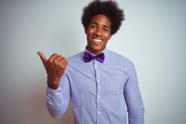 Afro iş adamı çizgili gömlek ve mor papyon takıyor. İzole edilmiş beyaz arka planda gülümsüyor. Gülümsüyor ve başparmağıyla yana bakıyor..