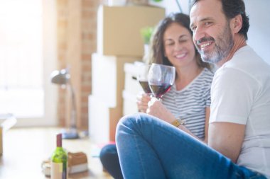 Orta yaş Senior romantik çift aşk yeni bir eve taşımak için mutlu gülümseyen bir bardak şarap içme kutluyor, etrafında kutuları ile daire katında oturan