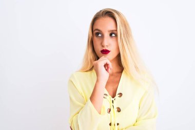 Zarif sarı tişört giyen genç ve güzel bir kadın izole edilmiş beyaz arka planda dikiliyor. Ciddi bir yüz ifadesi var. Soru sormayı düşünüyor.