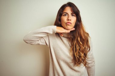 Kışlık süveter giyen genç bir kadın izole edilmiş beyaz arka planda durup boğazını bıçak niyetine kesiyor, saldırganlığı şiddetle tehdit ediyor.