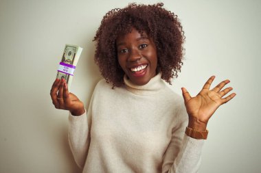 Yalnız beyaz arka planda dolarlar tutan Afrikalı genç bir kadın mutlu ve heyecanlı, kazanan ifade zaferi büyük bir gülümsemeyle kutluyor ve ellerini kaldırıyor.