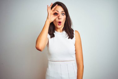 İzole edilmiş beyaz arka plan üzerinde duran genç ve güzel bir kadın. Şaşırmış yüz ifadesiyle şaşırmış, parmaklarının arasından bakan gözler. İnançsız ifade.