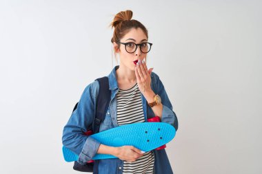 Sırt çantasıyla gezen kızıl saçlı bir kadın. İzole edilmiş beyaz arka plan üzerinde kaykay tutuyor. Ağzı kapalı.