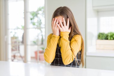 Genç, güzel sarışın kız evde günlük sarı süveter giyiyor. Ağlarken suratını ellerle kapatıyor. Depresyon kavramı.