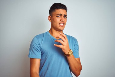 İzole edilmiş beyaz arka plan üzerinde duran mavi tişörtlü genç Brezilyalı adam tiksinti dolu ve tiksindirici bir yüz ifadesi takınıyor çünkü tiksinti tepkisi veriyor. Eller havada. Can sıkıcı bir kavram..