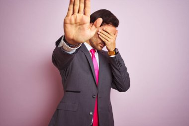 Takım elbiseli ve kravatlı genç yakışıklı bir işadamı yalnız pembe arka planda dikiliyor ellerle gözleri örtüyor ve üzgün ve korku ifadeleriyle jestleri durduruyor. Utanç verici ve olumsuz bir kavram..