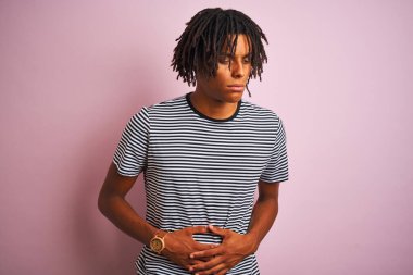 Rasta desenli tişörtlü Afro bir adam midesi bulanan, acı veren bir hastalık yüzünden izole edilmiş pembe arka planda duruyor. Ache kavramı.