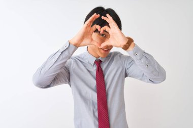 Çinli işadamı zarif bir kravat takıyor, izole edilmiş beyaz arka planda duruyor, elleriyle ve parmaklarıyla kalp şeklinde işaret diliyle bakıyor.