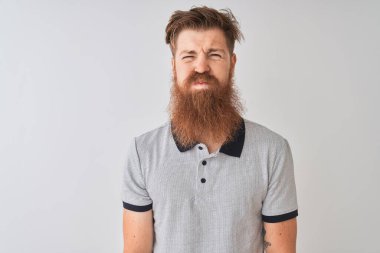 Gri polo giyen genç kızıl saçlı adam izole edilmiş beyaz arka planda durup komik yüzlü yanakları şişiriyor. Havayla şişmiş ağız, çılgın bir ifade..