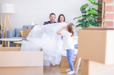 Güzel aile, anne-babalar kanepede kahve içme oturmuş karton kutular etrafında yeni evde oynayan çocuğuna bakıyor