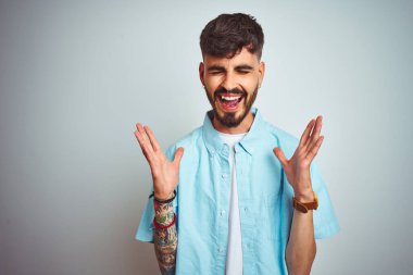 Mavi gömlekli genç adam, izole edilmiş beyaz arka planda duruyor. Kolları havada ve gözleri kapalı heyecanla haykırarak başarının çılgınlığını kutluyor. Kazanan konsept