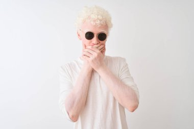 Ayrı beyaz arka planda tişört ve güneş gözlüğü takan genç albino sarışın adam yanlışlıkla elleri ile ağzını kapatarak şok etti. Gizli konsept.
