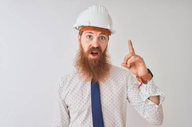 İzole edilmiş beyaz arka plan üzerinde güvenlik kaskı takan genç kızıl saçlı mimar başarılı bir fikir işaret ediyor. Heyecanlı ve mutlu. Bir numara..