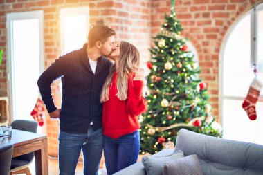 Mutlu ve kendinden emin gülümseyen genç bir çift. Evde Noel ağacının etrafında dikilip sarılıyorsun.