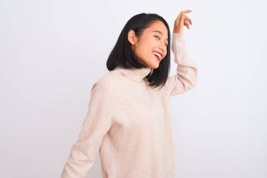 Balıkçı yaka kazak giyen genç bir kadın izole edilmiş beyaz arka planda duruyor mutlu ve neşeli dans ediyor, gülümsüyor hareketli ve kendinden emin bir şekilde müzik dinliyor.