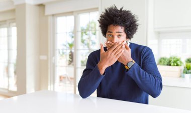 Genç Afro-Amerikan bir adam günlük süveter giyer evde oturur ağzı yanlışlıkla ellerle kapatırken şok geçirir. Gizli konsept.