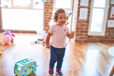 Genç, güzel bebek mutlu gülümsüyor. Anaokulunda yüzünde gülümsemeyle dikilirken