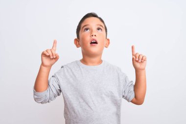 Gri günlük tişört giyen güzel bir çocuk beyaz arka planda dikiliyor şaşkın şaşkın bakıyor, parmaklarıyla işaret ediyor ve kollarını kaldırıyordu..