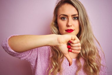 Pembe izole edilmiş arka plan üzerinde duran genç ve güzel bir kadın. Kızgın bir yüzü var. Eksi işareti var.