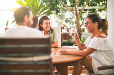 Güzel bir aile terasta oturmuş kahve içiyor, konuşuyor ve gülümsüyor.
