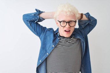 Genç albino sarışın adam kot gömlek ve gözlük takıyor beyaz arka planda çılgın ve elleri başında korkmuş, korkmuş ve ağzı açık şoktan şaşırmış.