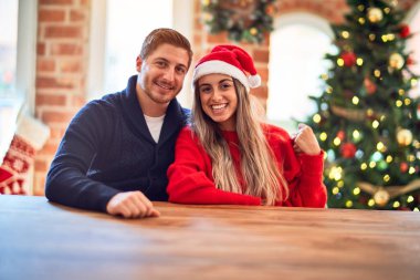 Mutlu ve kendinden emin gülümseyen genç bir çift. Noel ağacının etrafında sandalyede oturup, evde sarılıyorum.