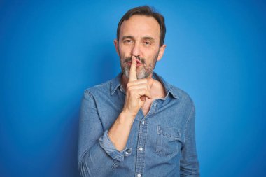 Gri saçlı, mavi arka planda yakışıklı, orta yaşlı bir adam sessiz olmak istiyor. Sessizlik ve gizli konsept.