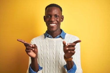 İzole edilmiş sarı arka planda kot gömlek ve beyaz kazak giyen Afro-Amerikalı adam farklı yönleri gösteren kendine güvenle gülümsüyor. Reklam için boşluk kopyala