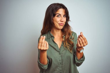 Yeşil tişörtlü genç bir kadın. Gri arka planda duruyor. Elleriyle para hareketi yapıyor.