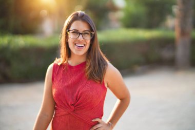 Genç ve güzel bir kız gülümseyerek mutlu ve kendinden emin bir şekilde parkta yürüyor, yüzünde bir gülümsemeyle duruyor.