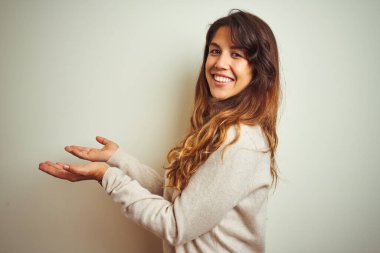 Kışlık süveter giyen genç bir kadın izole edilmiş beyaz arka planda duruyor. Elleri açık, fotokopi alanını gösteren avuç içleri açık, gülümseyerek mutlu bir gülümseme sunuyor.