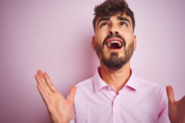 Dövme ile genç adam gömlek ayakta izole pembe arka plan çılgın ve deli çığlık ve agresif ifade ve silah ile bağırarak kaldırdı. Hayal kırıklığı kavramı.