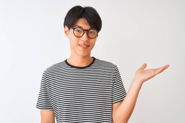 Gözlüklü ve donanma tişörtlü Çinli bir adam izole edilmiş beyaz arka planda dikiliyor neşeli bir şekilde gülümsüyor ve avuç içi kameraya bakıyor..