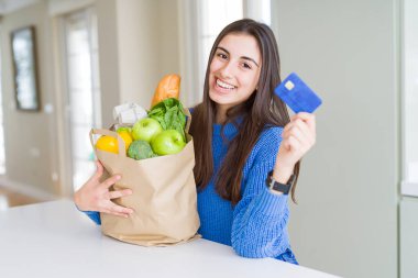 Taze bakkaliye ve gösteri dolu bir kağıt torba tutan genç kadın