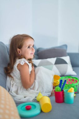 Sevimli sarışın bebek kanepede oturuyor evde yemek ve çatal bıçakla yemek pişiriyor.