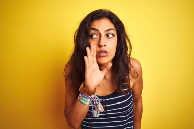 Çizgili tişört giyen genç ve güzel bir kadın izole edilmiş sarı arka planda duruyor. Ağızda gizli söylentiler dolaşıyor, kötü niyetli konuşmalar fısıldıyor.