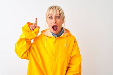 Sarı yağmurluk giyen orta yaşlı bir kadın izole edilmiş beyaz arka plan üzerinde durup başarılı bir fikir işaret ediyor. Heyecanlı ve mutlu. Bir numara..