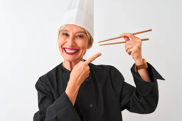 中年妇女厨师头戴帽子 拿着筷子顶着孤立的白色背景 非常高兴地用手和手指指指点点 — 图库照片