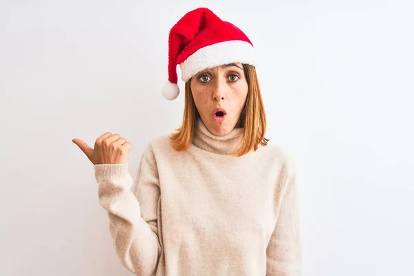 Hermosa Pelirroja Con Sombrero Navidad Sobre Fondo Aislado Sorprendido Señalando —  Fotos de Stock