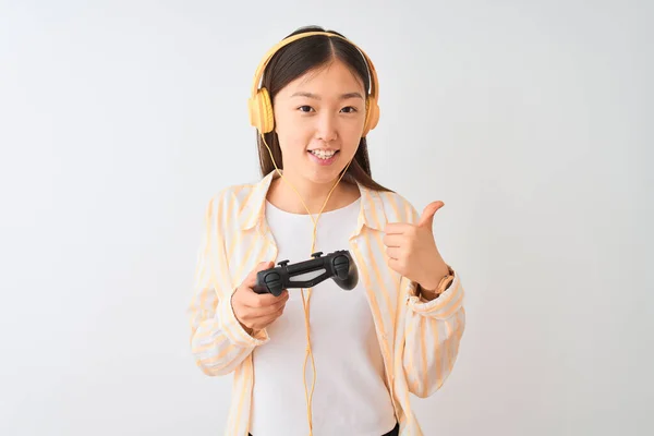 中国游戏玩家使用耳机玩电子游戏的女人在孤独的白色背景上开心地笑着做着好的手势 用手指竖起大拇指 很好的标志 — 图库照片