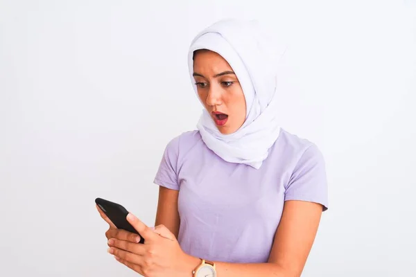 若いです美しいですアラビア人の女の子身に着けていますヒジャーブスマートフォンを使用して隔離された白い背景驚きの顔でショックで怖がっています 恐れと恐怖の表現で興奮 — ストック写真