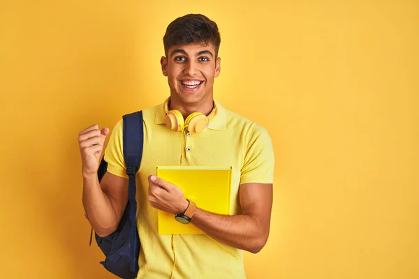 孤立した黄色の背景の上にバックパックのヘッドフォンノートブックを身に着けているインドの学生の男は誇りを叫び 勝利と成功を祝う非常に興奮し 応援感情 — ストック写真
