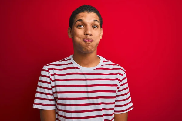 Mladý Pohledný Arabský Muž Pruhovaným Tričkem Izolovaném Červeném Pozadí Nafouknutými — Stock fotografie