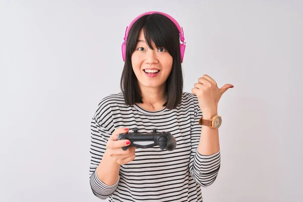 中国游戏女玩家用耳机在孤立的白色背景下玩电子游戏 手指朝天 笑容满面 — 图库照片