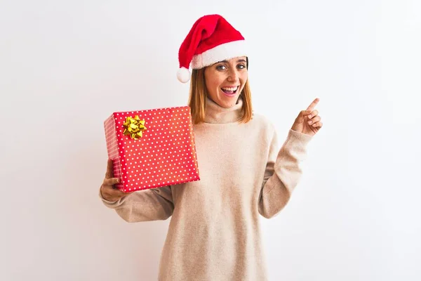 Schöne Rothaarige Frau Mit Weihnachtsmütze Hält Geschenk Über Isoliertem Hintergrund — Stockfoto