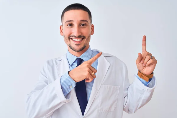 年轻的医生 身穿白衣 面带微笑 望着摄像机 用双手和手指指向旁边 — 图库照片