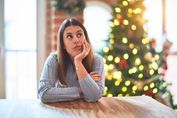 若いです美しい女性座っているテーブルに家の周りのクリスマスツリーと装飾思考疲れていると退屈でうつ病の問題と一緒に交差腕 — ストック写真