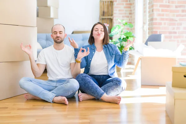 Karton kutuların etrafında oturan genç çift yeni bir eve taşınıyor rahatlıyor ve gözleri kapalı meditasyon yaparken parmaklarıyla gülümsüyor. Yoga konsepti.