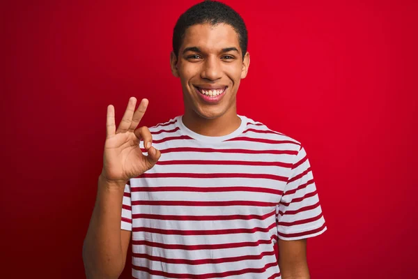 年轻英俊的阿拉伯男子穿着条纹T恤 披着孤立的红色背景 微笑着 手指手画脚地签了名 成功表达 — 图库照片